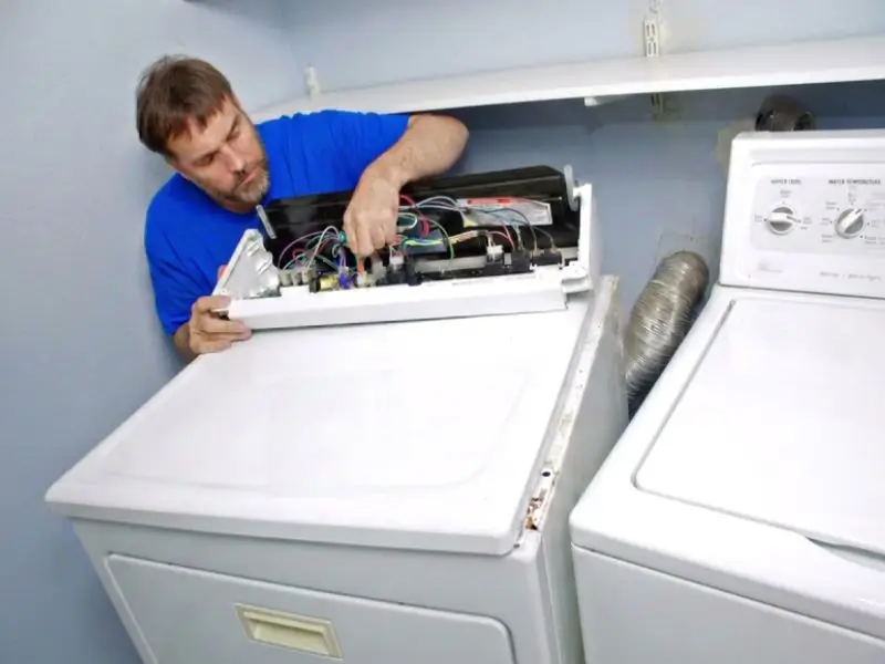 Dryer repair technician in blue t-shirt is busy doing his job.