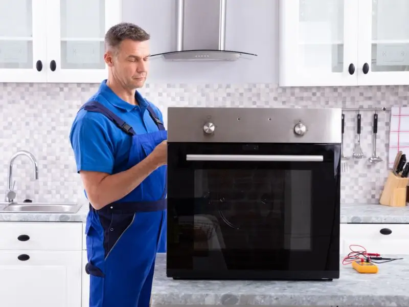 Oven repair technician in a blue workwear stays next to the wall oven.
